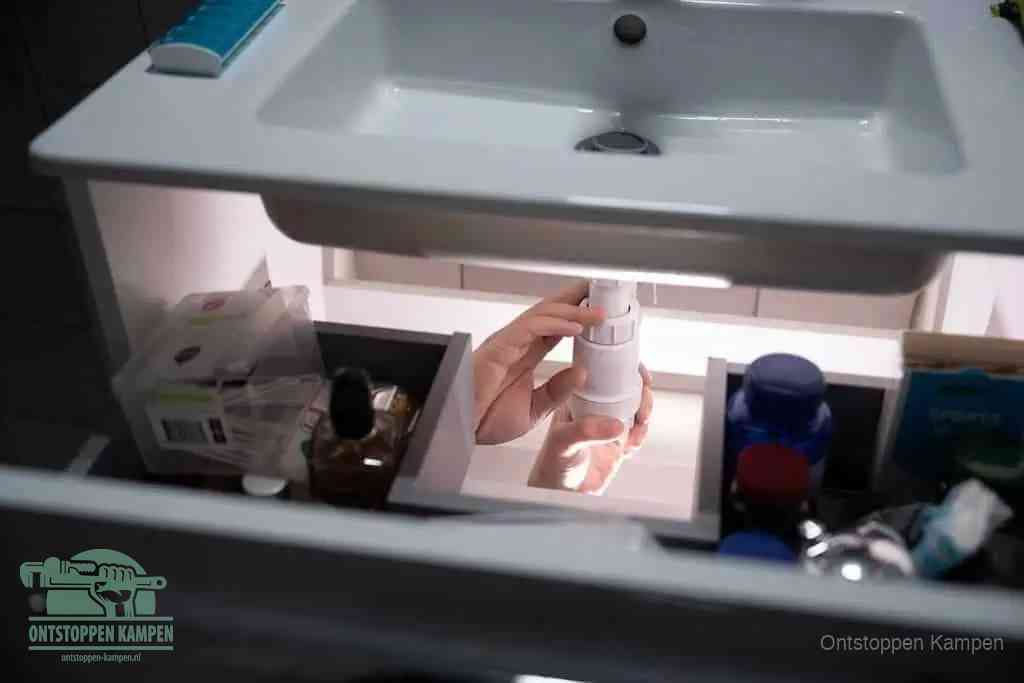 Een pompfles met zeep boven een wastafel, de heet water en afwasmiddel-methode om een vetprop in de afvoer los te maken in Kampen