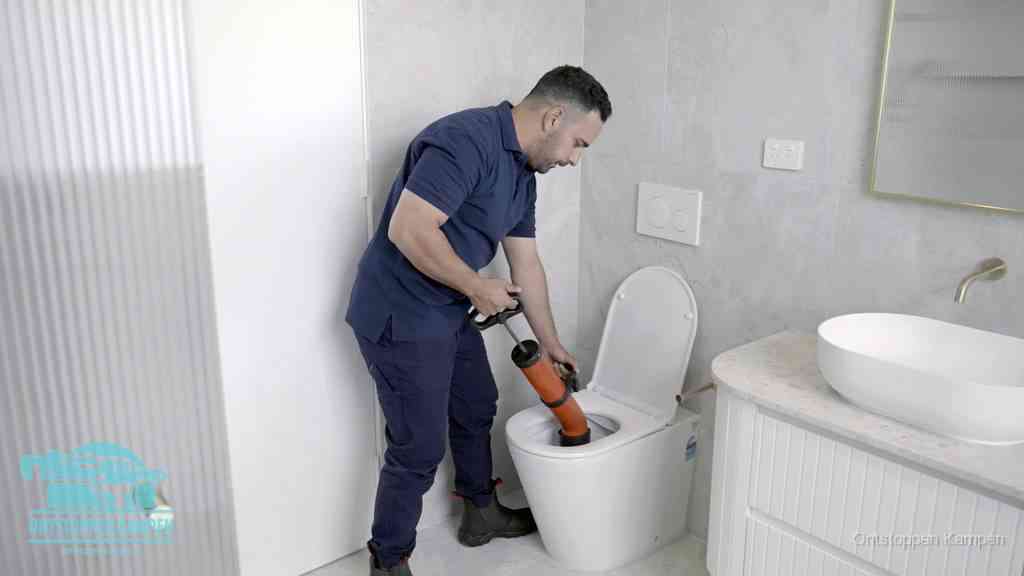 Een monteur buigt over een wandcloset en duwt met de hand een persluchtontstopper in de toiletpot om de verstopping handmatig los te maken in Kampen