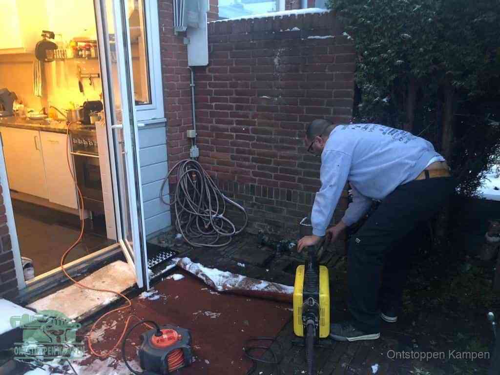 Een monteur werkt buiten bij een open riool-/grondput met een elektrische ontstoppingsmachine om een verborgen afvoerprobleem op te sporen in Kampen
