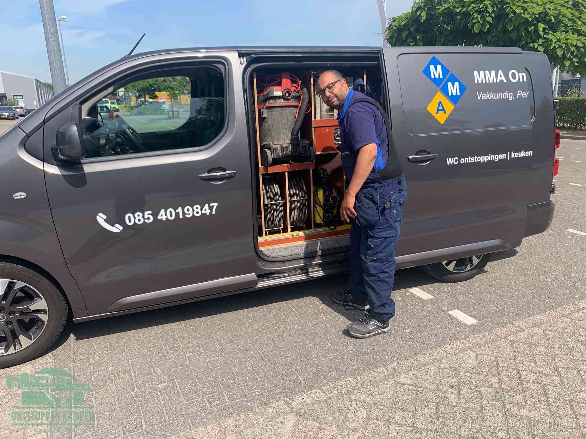 Een monteur bij de open schuifdeur van zijn bedrijfsbus op een parkeerplaats, klaar om de oorzaak van terugkerende afvoerverstoppingen aan te pakken in Kampen
