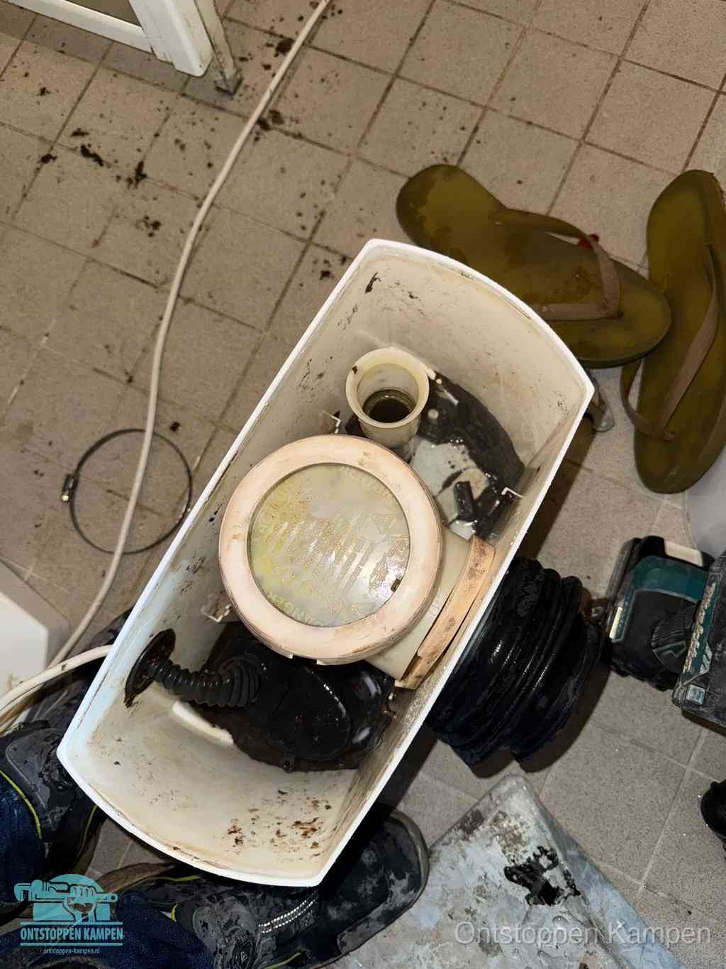 Een gedemonteerde toiletpot op de vloer met ontstoppingsveer en gereedschap ernaast, het verwijderen van een vastzittend voorwerp uit de wc in Kampen