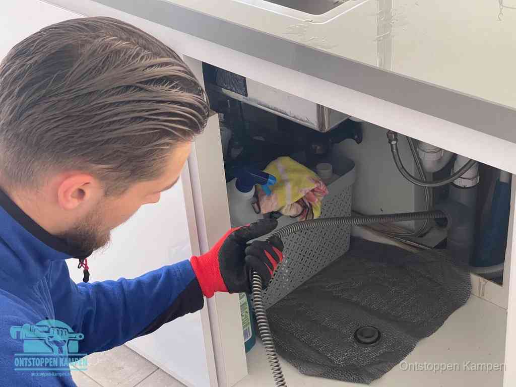 Een monteur voert een flexibele ontstoppingsveer in de afvoer om een verstopping voorbij de bocht van het toilet te bereiken in Kampen