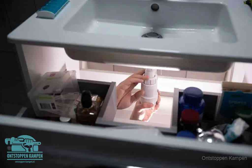 Een pompfles met zeep boven een wastafel in de toiletruimte, de warm water en afwasmiddel-methode om de wc te ontstoppen in Kampen