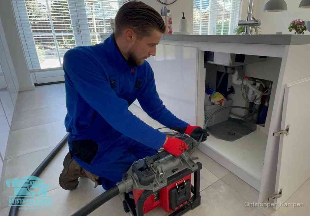 Een monteur voert een professionele elektrische ontstoppingsmachine in de afvoer onder de spoelbak tijdens het gootsteen ontstoppen in Kampen