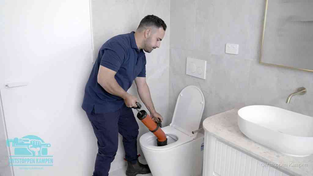 Een monteur gebruikt een handmatige perspomp (toiletontstopper) op een wandcloset tijdens het professioneel wc ontstoppen in Kampen