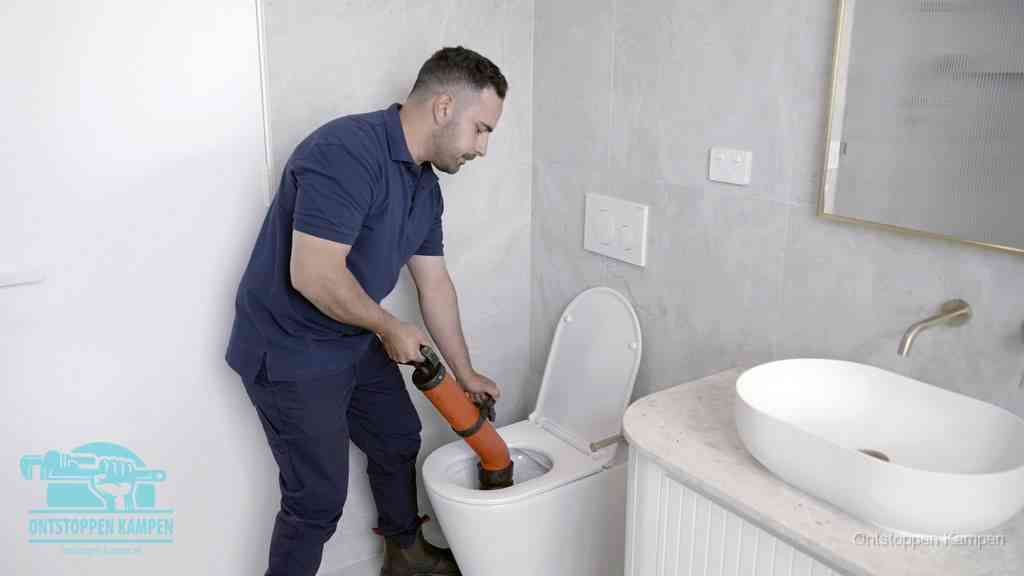 Een man gebruikt een handmatige luchtdruk-ontstopper in een modern betegeld toilet om zelf de wc te ontstoppen in Kampen